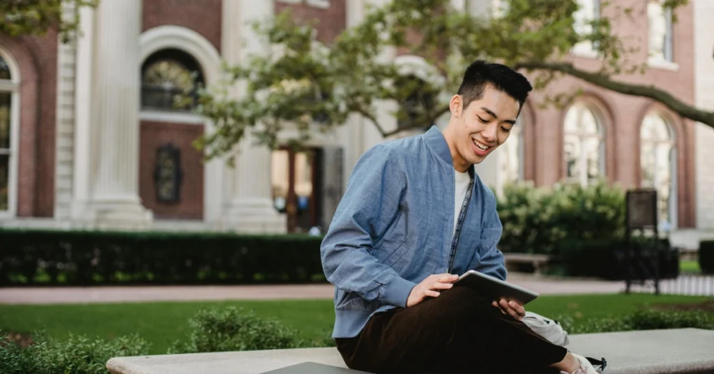 student using tablet while resting on bench in park
