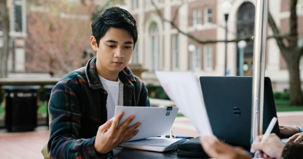 A Student in Plaid Long Sleeves Reading Papers at Campus