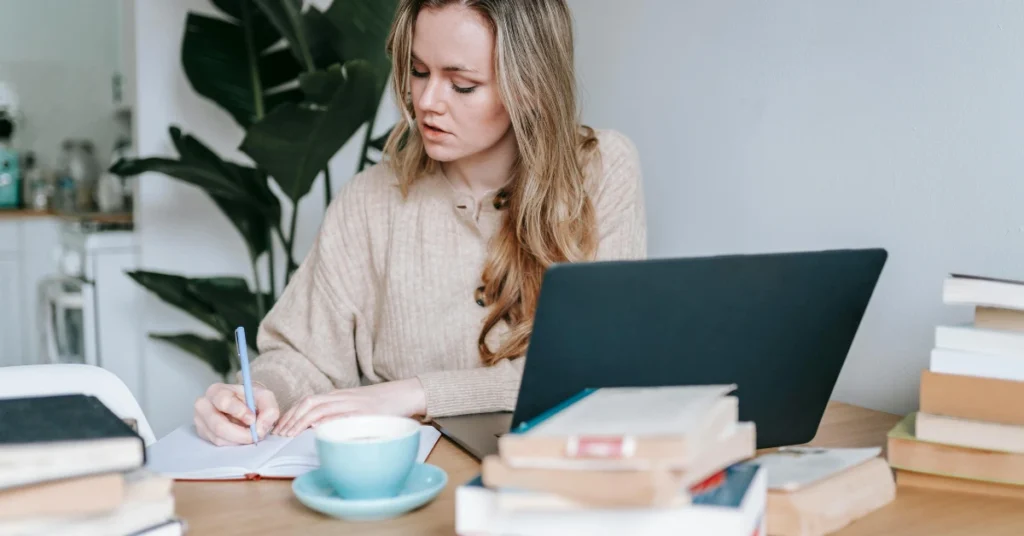 Student Writing in Notebook Near Laptop and Coffee