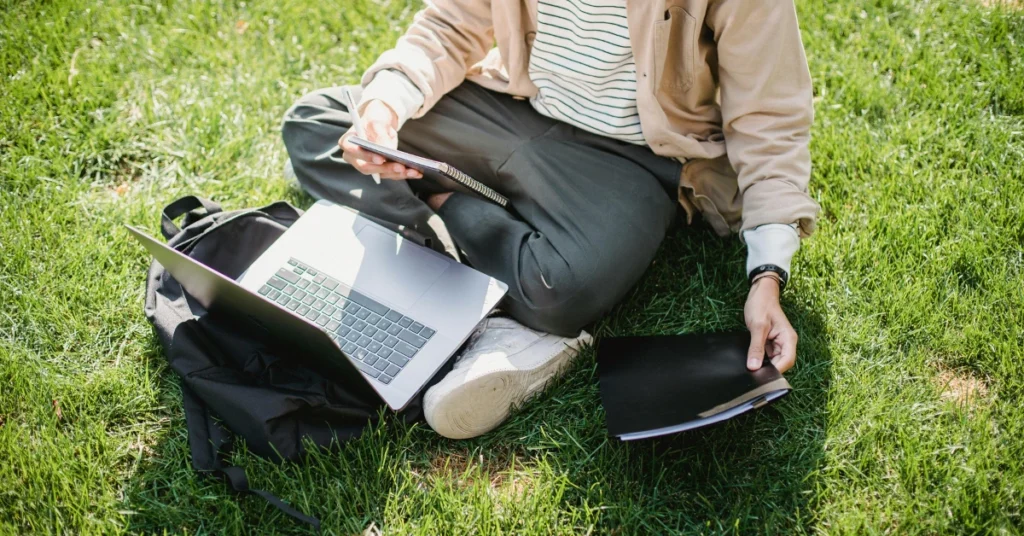 student with laptop and notebook studying in park