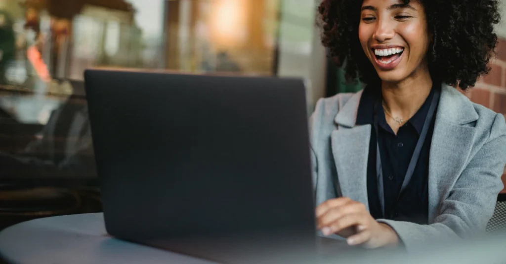 Student in gray blazer smiling while using a laptop
